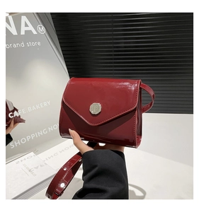 Détail d'un petit sac bandoulière en cuir verni rouge foncé avec boucle argentée au café