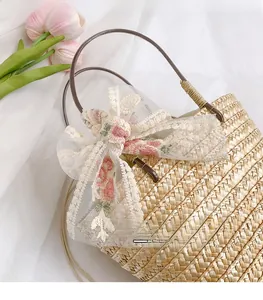 Close-up of woven straw bucket bag featuring a white lace bow and pink floral embroidery