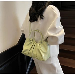 Detail of pistachio green pleated handbag worn crossbody showing smooth oil wax leather texture