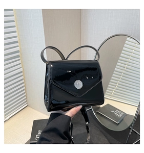 Détail du sac à bandoulière en cuir verni noir minimaliste avec emblème argenté et brillant