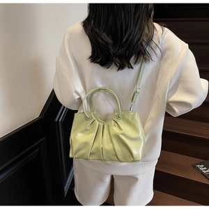 Detail of pistachio green pleated handbag with leather strap shown in a casual lifestyle setting