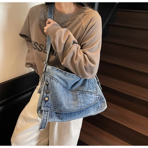 Close-up of washed denim crossbody bag featuring vintage metal rivets and flap design