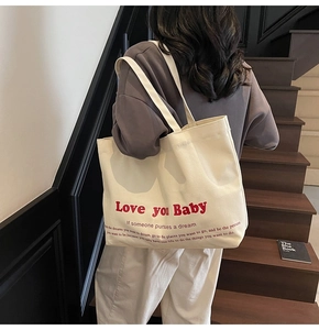 Detail of a creamy canvas tote bag with red 'Love you Baby' text and black lettering