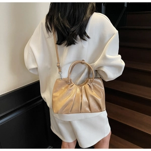 Close-up of beige gold pleated handbag with soft glossy finish and shoulder strap