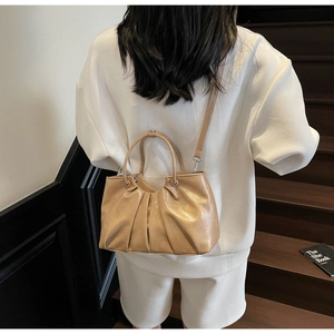 Rear view of a model carrying a beige pleated handbag with glossy oil wax leather finish