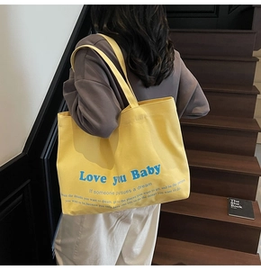 Detailed macro view of large yellow canvas tote bag with blue Love You Baby printed text