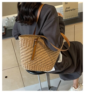 Detailed view of woven straw tote bag featuring brown leather handles and metal rivets