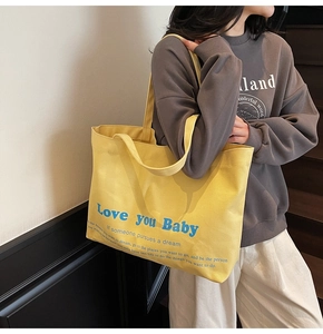 Detail of a bright yellow canvas tote bag with blue artistic typography and sturdy straps