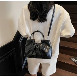 Detail of black pleated shoulder bag featuring glossy oil wax leather and silver hardware