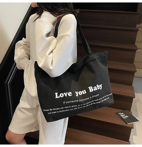 Detail of large black canvas tote bag with white lettering on a model at stairs