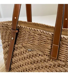 Detail of bohemian straw tote bag showing brown leather strap with contrast white stitching