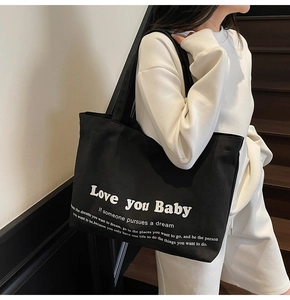 Close-up of black canvas tote bag with Love You Baby print on a female shoulder