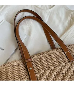 Close-up of hand-woven straw tote bag with brown leather strap and silver metal rivets