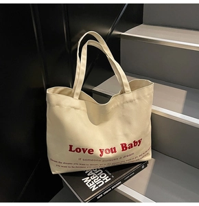 Detail shot of cream canvas tote bag featuring bold red Love you Baby printed text