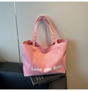 Detail of pink canvas tote bag with white artistic lettering on a black leather sofa