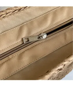 Detail view of the silver metal zipper and canvas lining on a brown woven straw tote bag