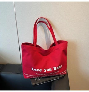 Detail of red cotton canvas tote bag with Love you Baby text on black sofa background