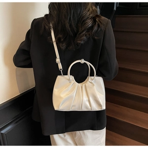 Detail view of white pleated dumpling bag with ring handles and adjustable strap
