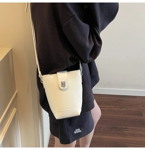 Close-up of a white lychee grain leather bucket bag with a metal twist lock and slim strap