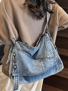 Vintage blue denim tote bag with metal rivets and wide strap shown on a shoulder
