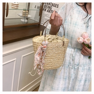 Close-up of hand-woven straw bucket bag featuring a floral scarf and pearl keychain
