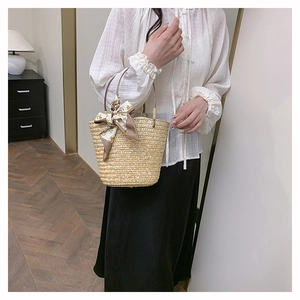 Detail view of woven straw bucket bag with floral scarf handle and round dark brown grip