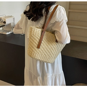 Detail of handwoven straw tote bag with brown leather straps in a cafe setting