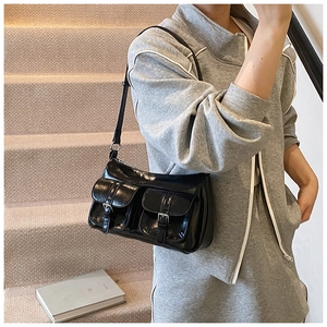 Detail of black glossy shoulder bag featuring double pockets and silver metal buckles