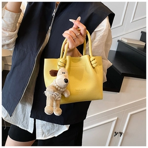 Detail of yellow lychee pattern leather bucket bag with woven handle and plush charm