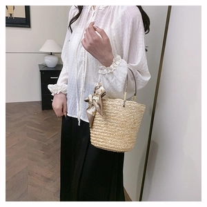 Detailed texture of woven straw bucket bag with elegant geometric print silk scarf handle