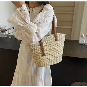 Detail of woven straw tote bag with brown leather straps worn with white lace dress