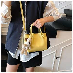 Detail of yellow lychee grain leather bucket bag featuring a cute plush dog charm