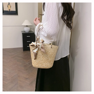 Detail of hand-woven straw bucket bag featuring a yellow floral silk scarf accent handle