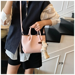 Detail of pink lychee texture bucket bag with cute puppy plush charm and brand logo