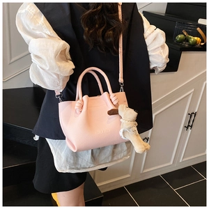 Detail of pink lychee leather bucket bag with cute plush dog pendant and embossed logo