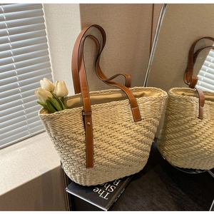 Close-up of woven straw tote bag with thin brown leather straps and striped texture