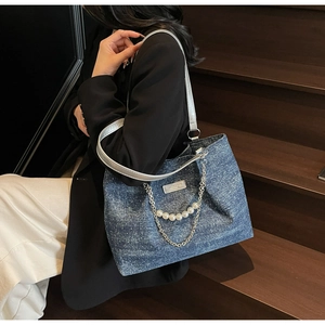 Detail der blauen Denim-Einkaufstasche mit silbernem Gurt und Perlenketten-Anhänger