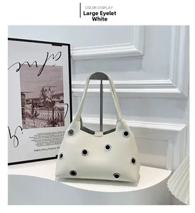 Detail of cream white leather underarm bag featuring large decorative silver metal eyelets