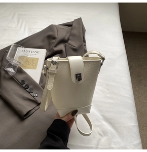 Detail of cream white bucket bag featuring litchi grain texture and silver metal clasp
