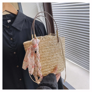 Detail of woven straw bucket bag featuring a silk scarf, pearl charm, and metal handles