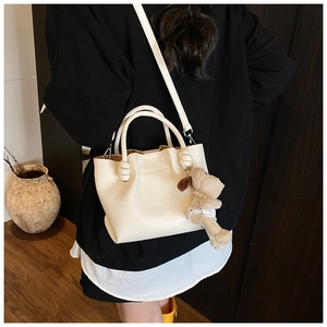 Detail view of white lychee grain bucket bag with ZSYB BAGS embossing and plush dog charm