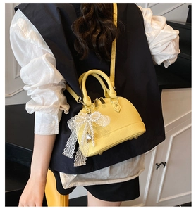 Detail of yellow shell-shaped handbag featuring lychee texture and pearl lace charm