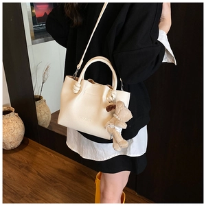 Close-up of litchi pattern cream bucket bag with brand logo and plush dog charm