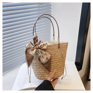 Detail of woven straw bucket bag with floral scarf and drawstring lining on white books