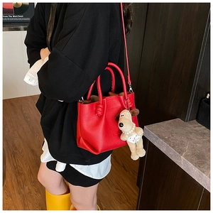 Detail view of red lychee leather tote bag with creative plush dog charm and shoulder strap