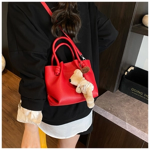 Red lychee textured bucket bag with cute plush dog charm shown in a lifestyle street shot
