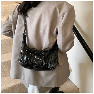 Detail der schwarzen Lackleder-Schultertasche mit Kreuzschnürung und Metallösen