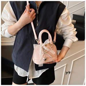 Close-up of pink shell bag with white lace bow, pearl chain and silver heart charm detail