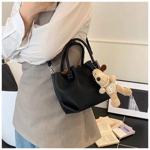Detail of black litchi texture handbag with cute dog charm and pearl necklace decoration