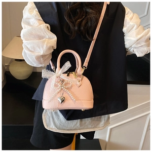 Pink shell bag with lace bow and pearl chain shown on a model in a cozy indoor setting